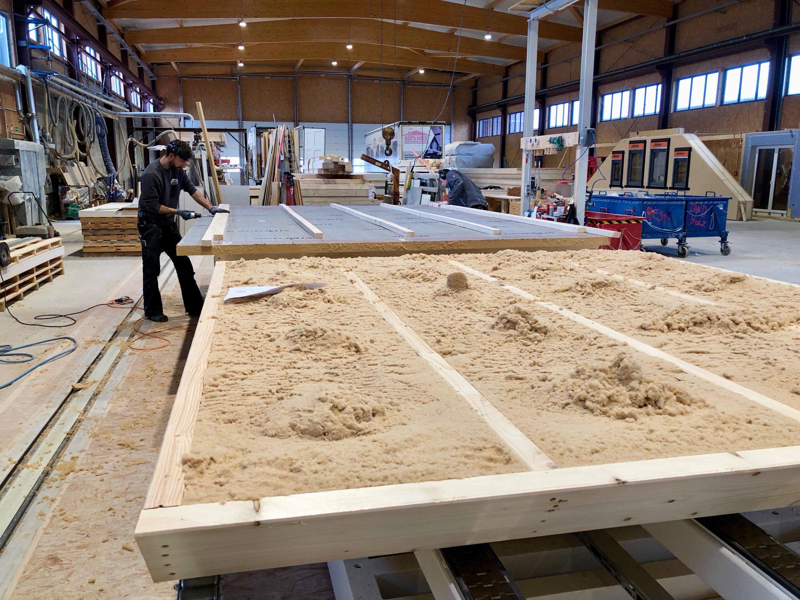 Während die beiden Mitarbeiter noch die Holzrahmen vorbereiten, steht im hinteren Teil der Halle schon der LKW für den Transport bereit (Foto: Eric Sturm)